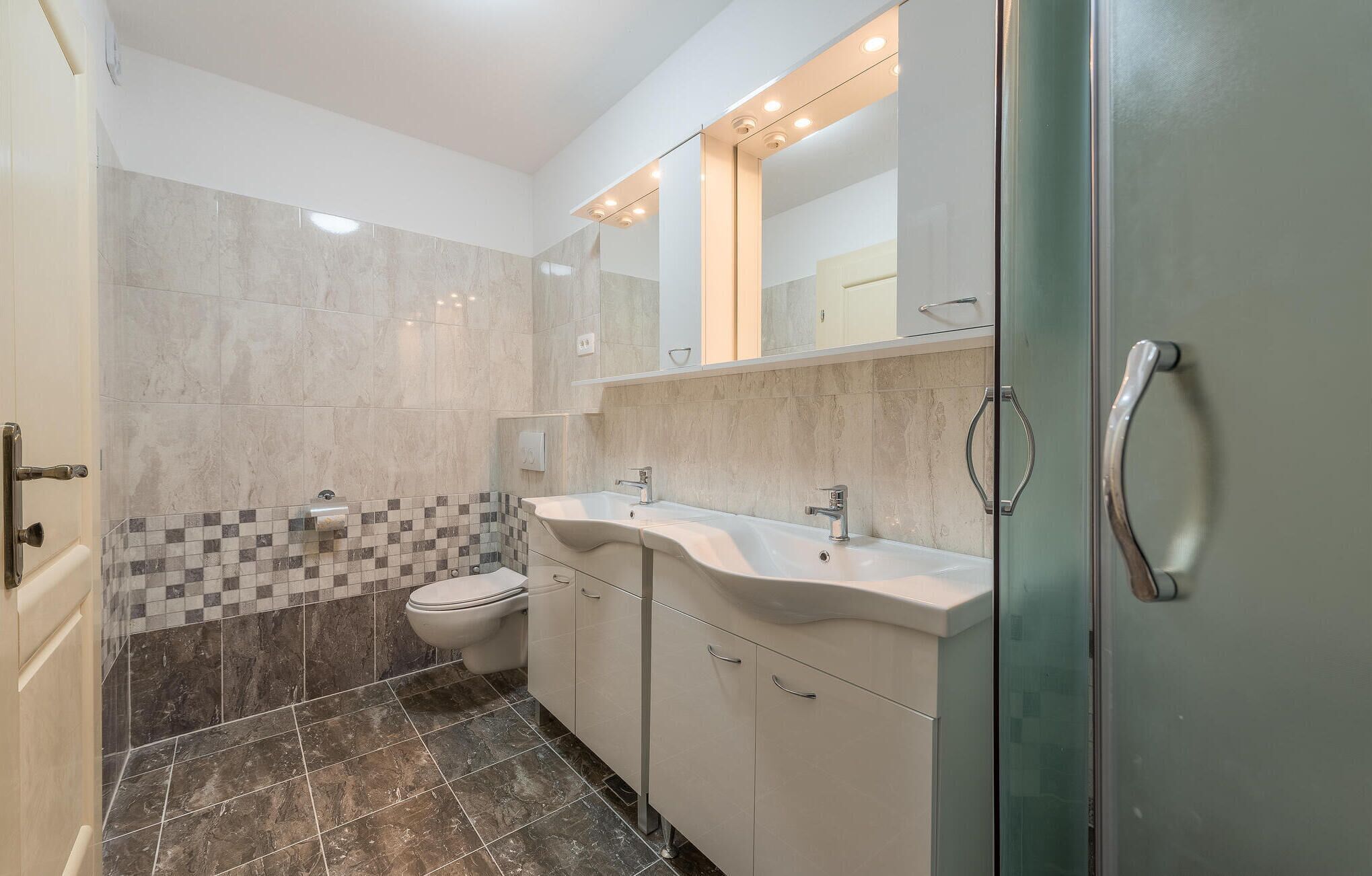 Een moderne badkamer met toilet, twee wastafels en een douchecabine.