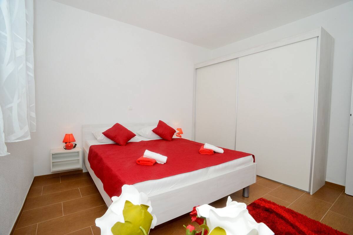 A neatly arranged bedroom with a bed, white nightstands, a red rug, and a wardrobe.