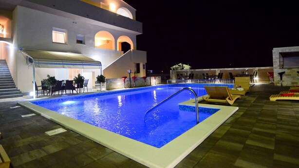 Una piscina con una zona hundida, rodeada de sillas de descanso y un área de estar techada.