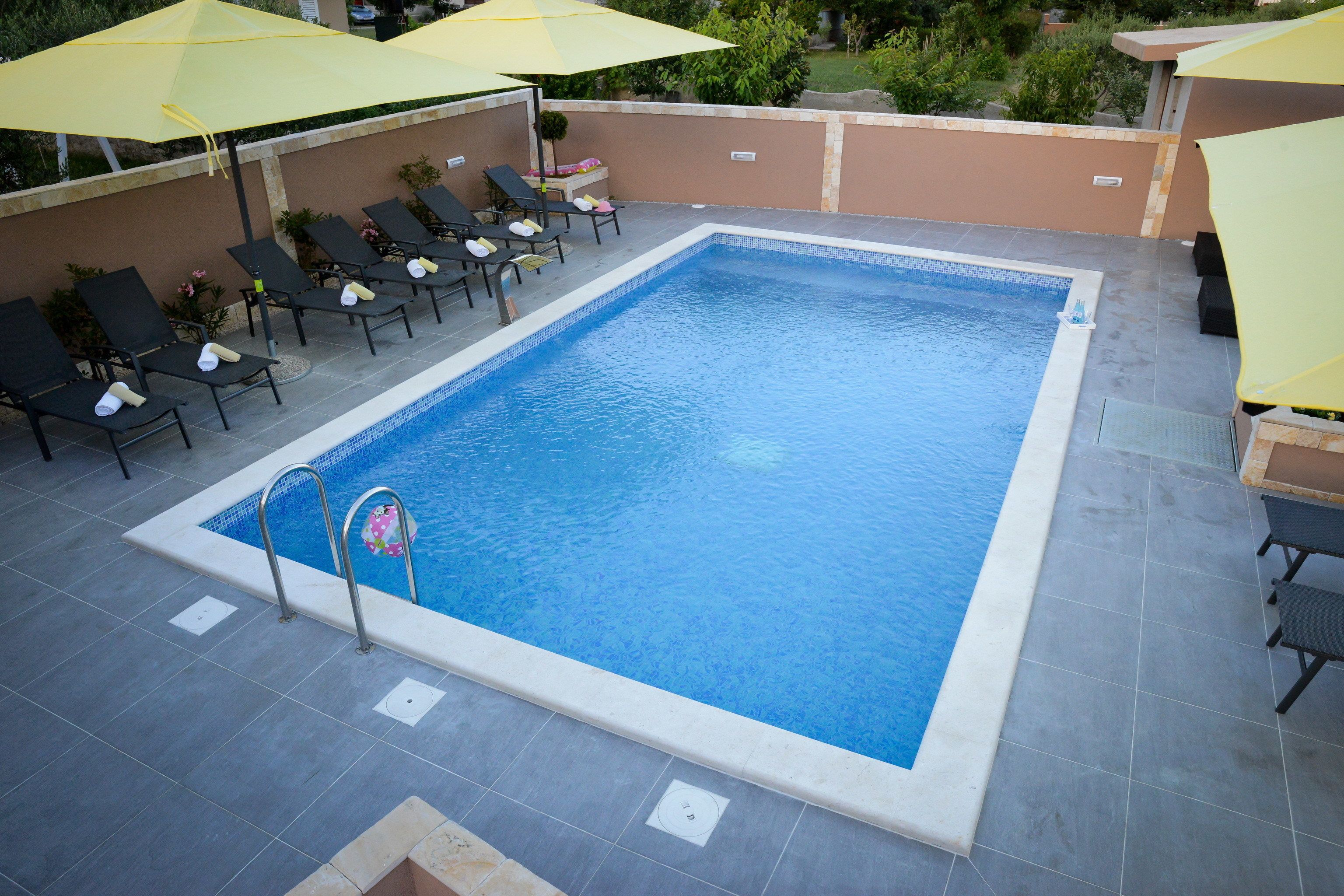 Piscina retangular com deck ladrilhado, rodeada por espreguiçadeiras e guarda-sóis amarelos.