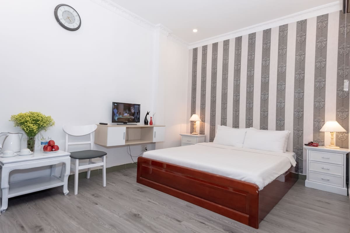 A modern hotel room with a large bed, a desk, a chair, and a TV.