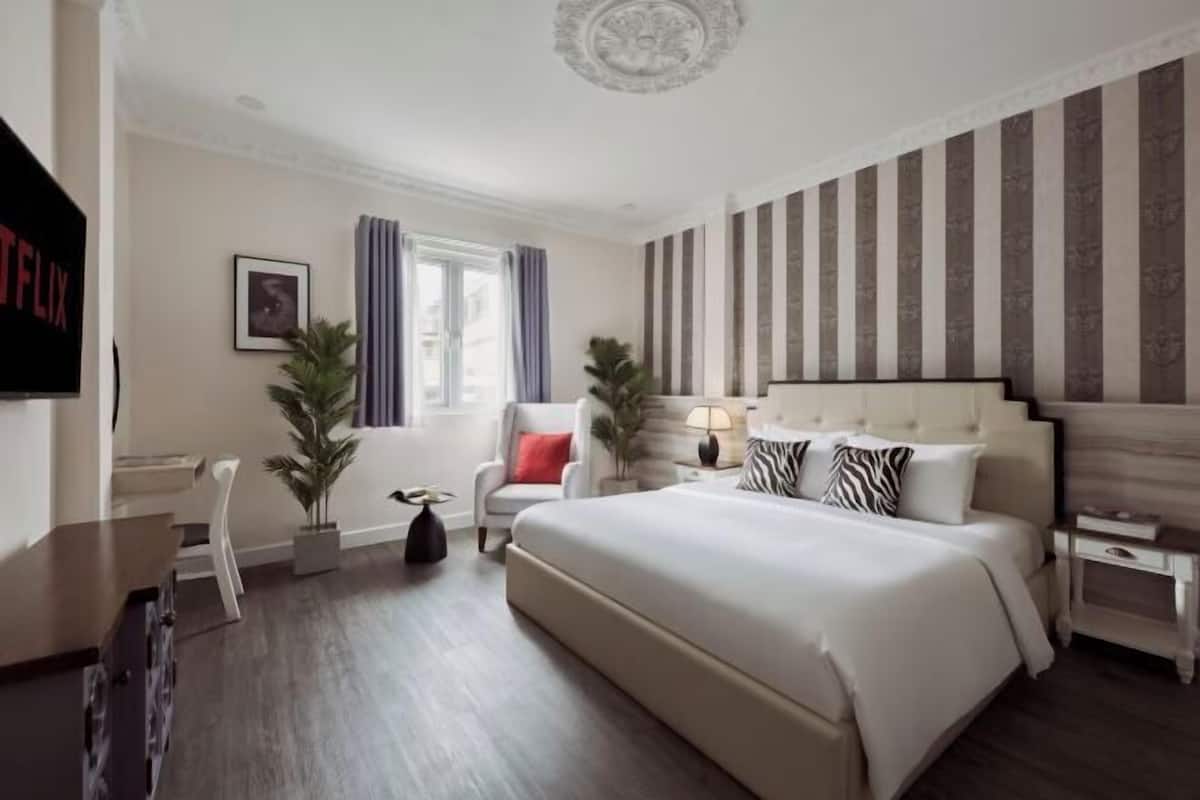 A hotel room with a large bed, a desk, a chair, a TV, and a window with curtains.