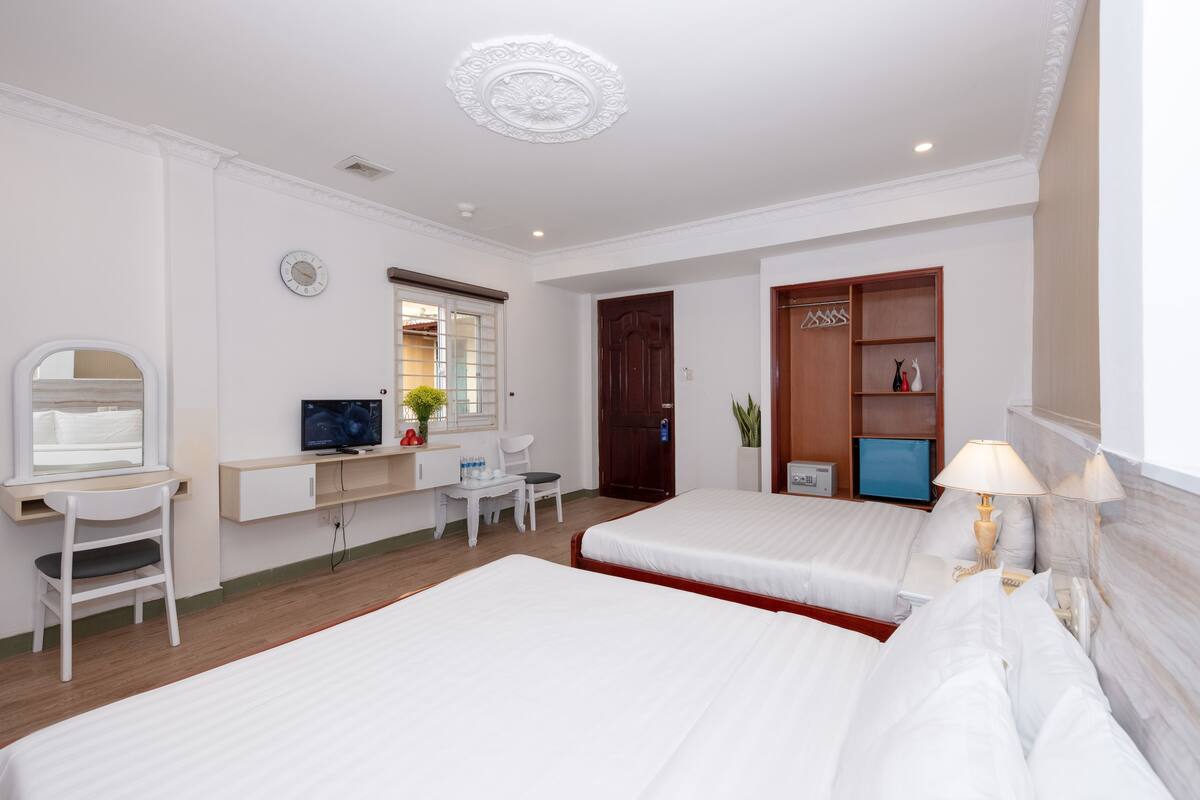 A hotel room with two beds, a desk with a chair, a TV, and a wardrobe.