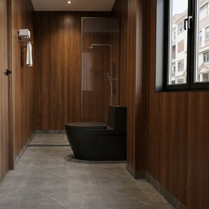 Un baño moderno con paneles de madera, una bañera negra y un ventanal con vistas a edificios.