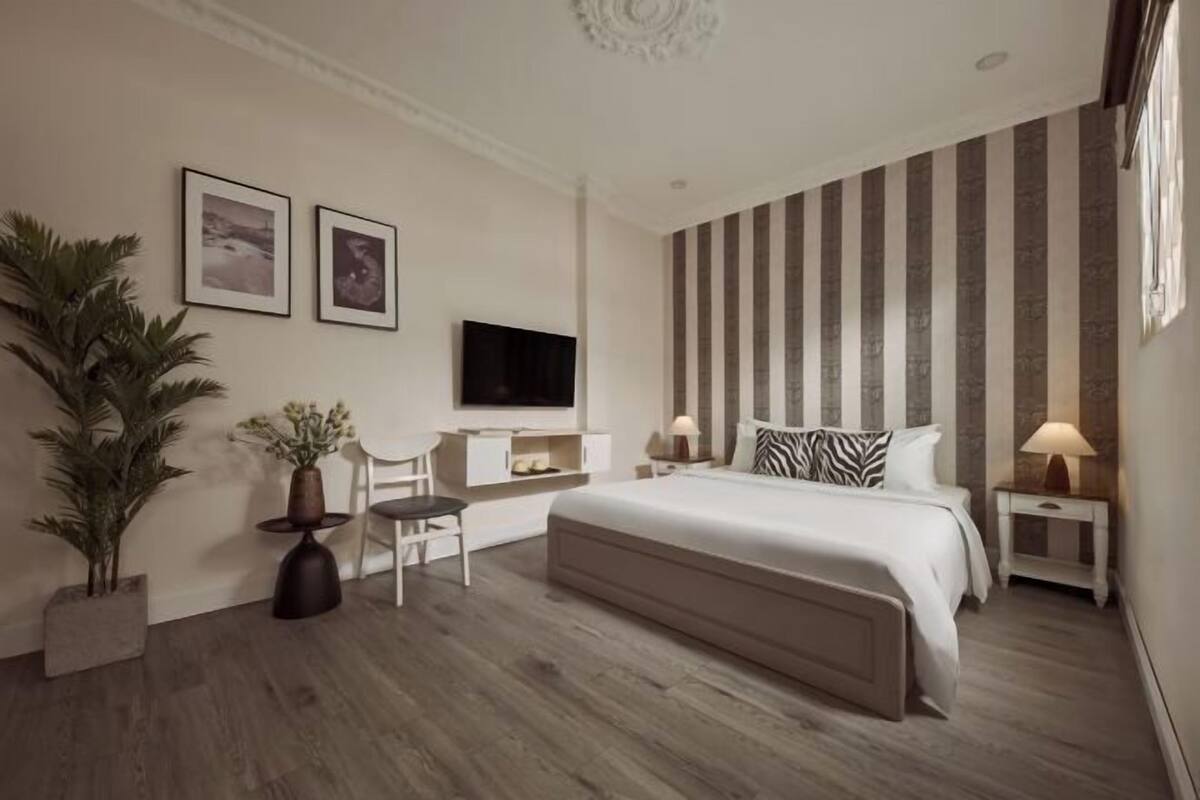 A bedroom with a bed, a desk, a chair, a TV, and a large plant.