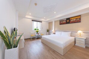 A modern hotel room with a large bed, a bedside table with a lamp, a small desk with a chair, and a potted plant. - The One Hotel Ben Thanh (Ho Chi Minh City)