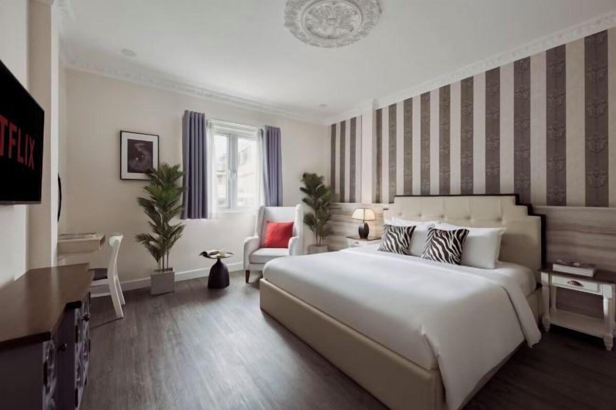 Una habitación de hotel con una cama grande, un escritorio, una silla, un televisor y una ventana con cortinas.