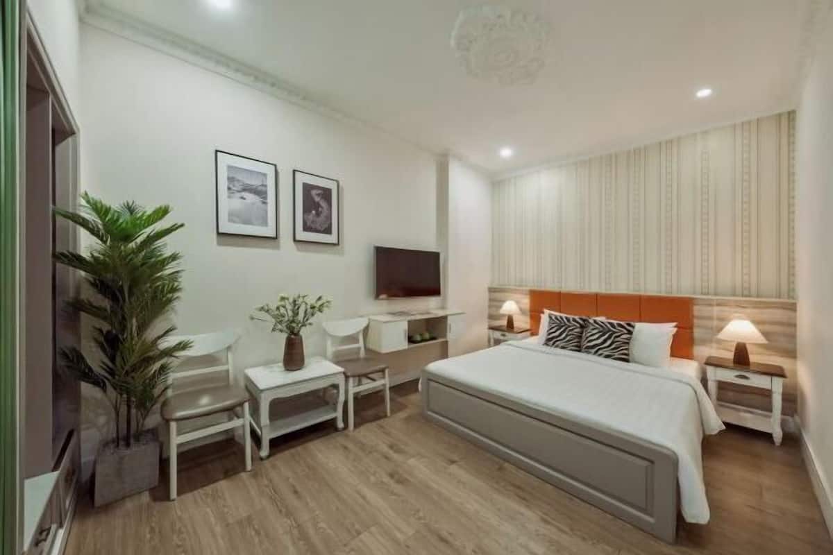 A modern hotel room with a bed, bedside tables, a TV, a desk, and a chair.