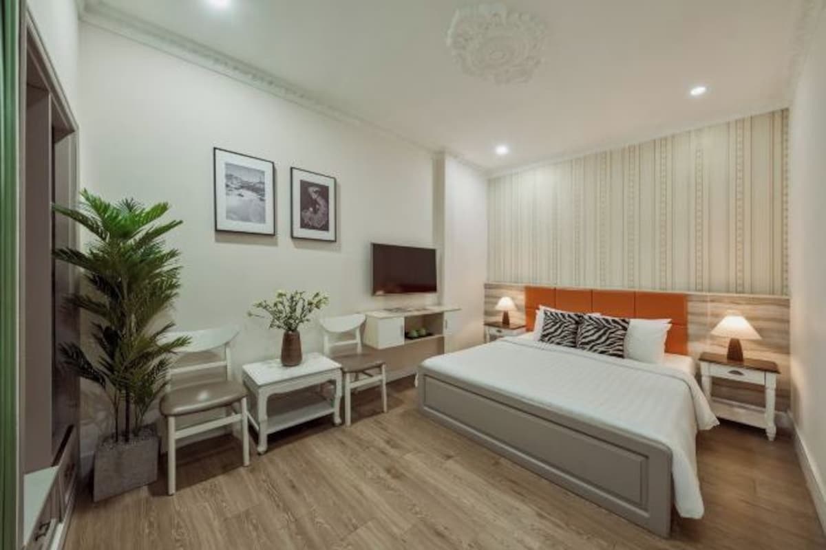 A modern hotel room with a bed, bedside tables, a TV, a desk, and a chair.