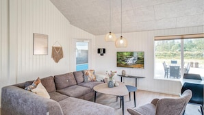 Ein Wohnzimmer mit einer Eckcouch, einem kleinen runden Tisch und einem an der Wand montierten Fernseher.