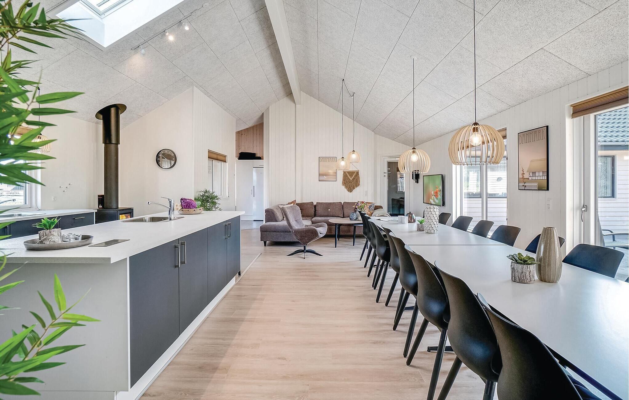 A modern kitchen with a central island, a dining area with a long table and chairs, and a living area with a sofa and a coffee table.