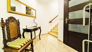 A wooden bench with a woven backrest, a small table, a mirror with a gold frame, and a dark wooden door with a glass panel. - Apartamenty EverySky Luxor Karkonoska (Karpacz)