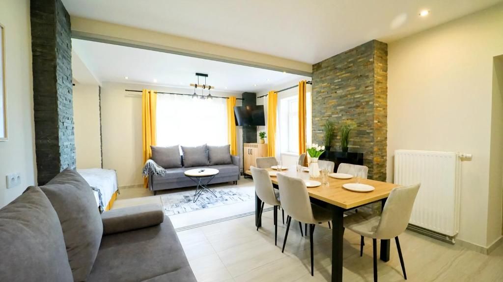 A modern living room with a sofa, dining table, and chairs. There is a fireplace and a stone wall.