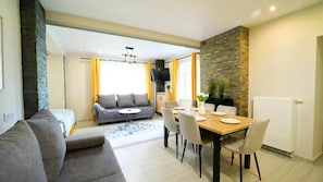 A modern living room with a sofa, dining table, and chairs. There is a fireplace and a stone wall. - Apartamenty EverySky Luxor Karkonoska (Karpacz)