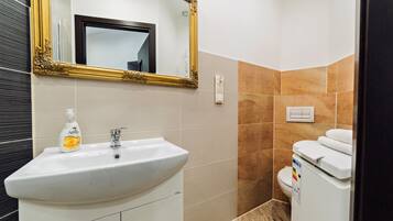 Un baño con un lavamanos blanco, un espejo con marco dorado y un inodoro con un adhesivo de arcoíris.