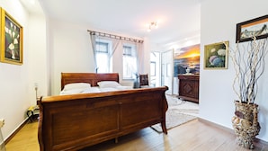 A bedroom with a wooden bed, a large window with sheer curtains, a view of the city, and a decorative vase on the floor. - Apartamenty EverySky Luxor Karkonoska (Karpacz)