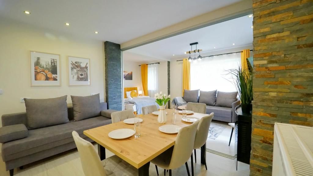 Una sala de estar moderna con comedor, que incluye un conjunto de sofás, una mesa de comedor con sillas y un amplio ventanal que proporciona luz natural.