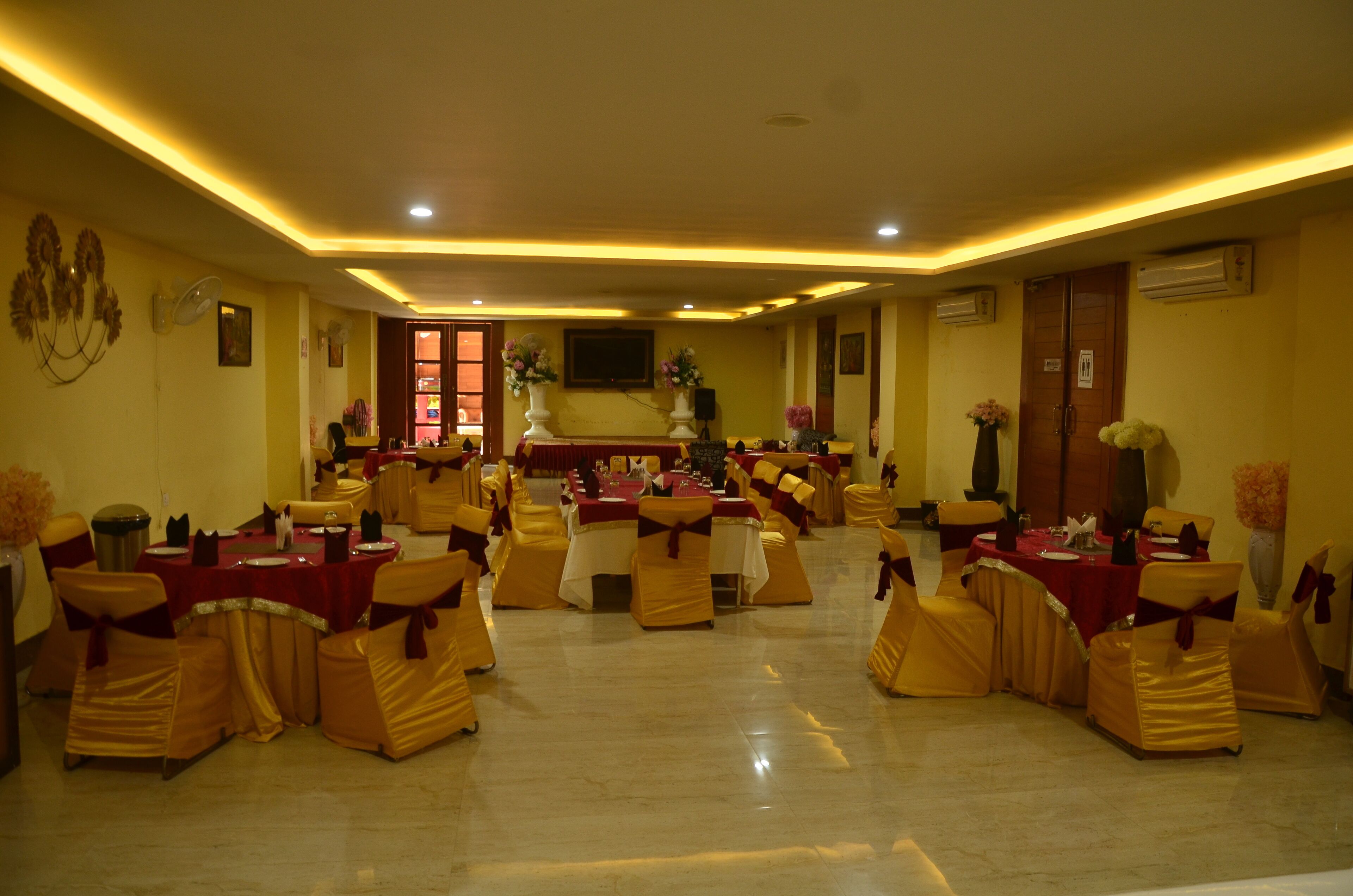 Un salón de banquetes con mesas y sillas redondas, un escenario y elementos decorativos.