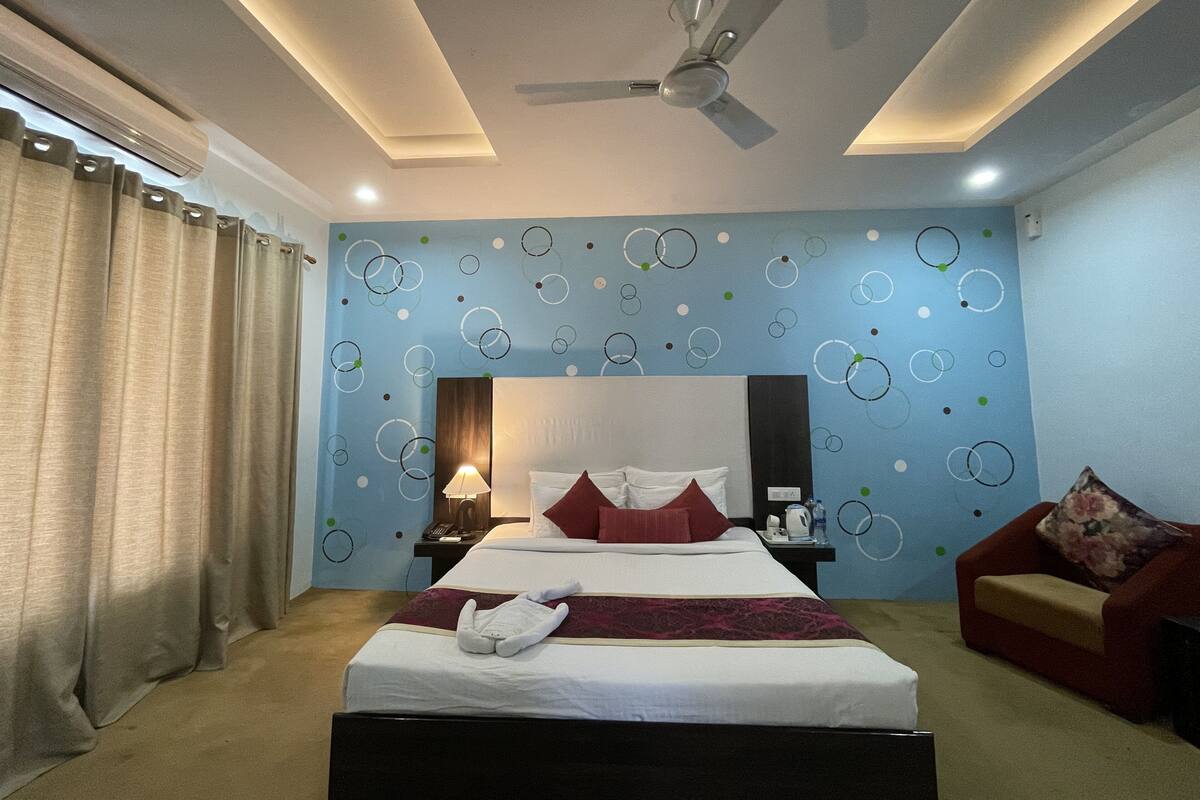 A hotel room with a bed, a ceiling fan, a nightstand, a red sofa, and a wall with circular patterns.
