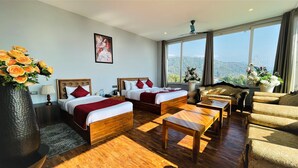 A hotel room with two beds, a sofa, a coffee table, and a large window offering a mountain view. - Sterling Banquet and Hotel (Palampur)
