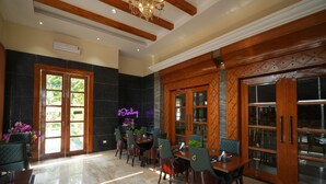 A spacious lobby with a marble floor, wooden paneling, and a chandelier. There are several tables and chairs arranged for dining or waiting. - Sterling Banquet and Hotel (Palampur)