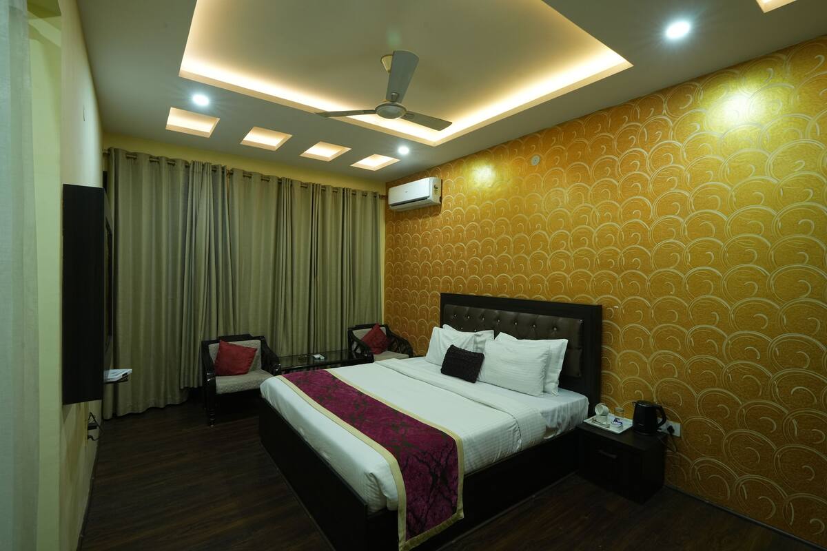 A hotel room with a large bed, a ceiling fan, recessed lighting, a wall air conditioner, and a patterned wallpaper.