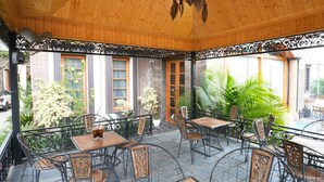 An outdoor patio with wooden tables and chairs, surrounded by a wooden ceiling and metal railings. - Sterling Banquet and Hotel (Palampur)