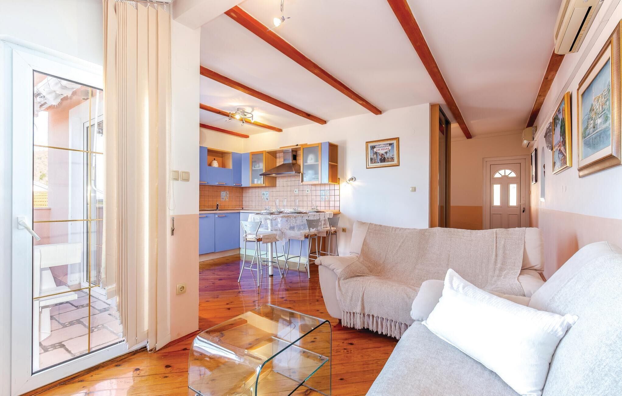 Una sala de estar moderna con una mesa de centro de vidrio, un sofá y una cocina al fondo.