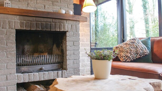 Una habitación acogedora con chimenea de ladrillo, una mesa de madera y un sofá de cuero con un cojín verde.