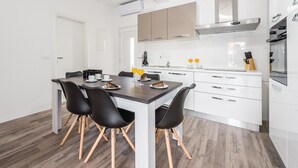 Una cocina moderna con armarios blancos, una campana extractora de acero inoxidable y un comedor con una mesa de madera oscura y sillas negras.