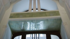 Una stanza con una panca a forma di arco, una parete inferiore rivestita di piastrelle verdi e un soffitto bianco con motivo a griglia.