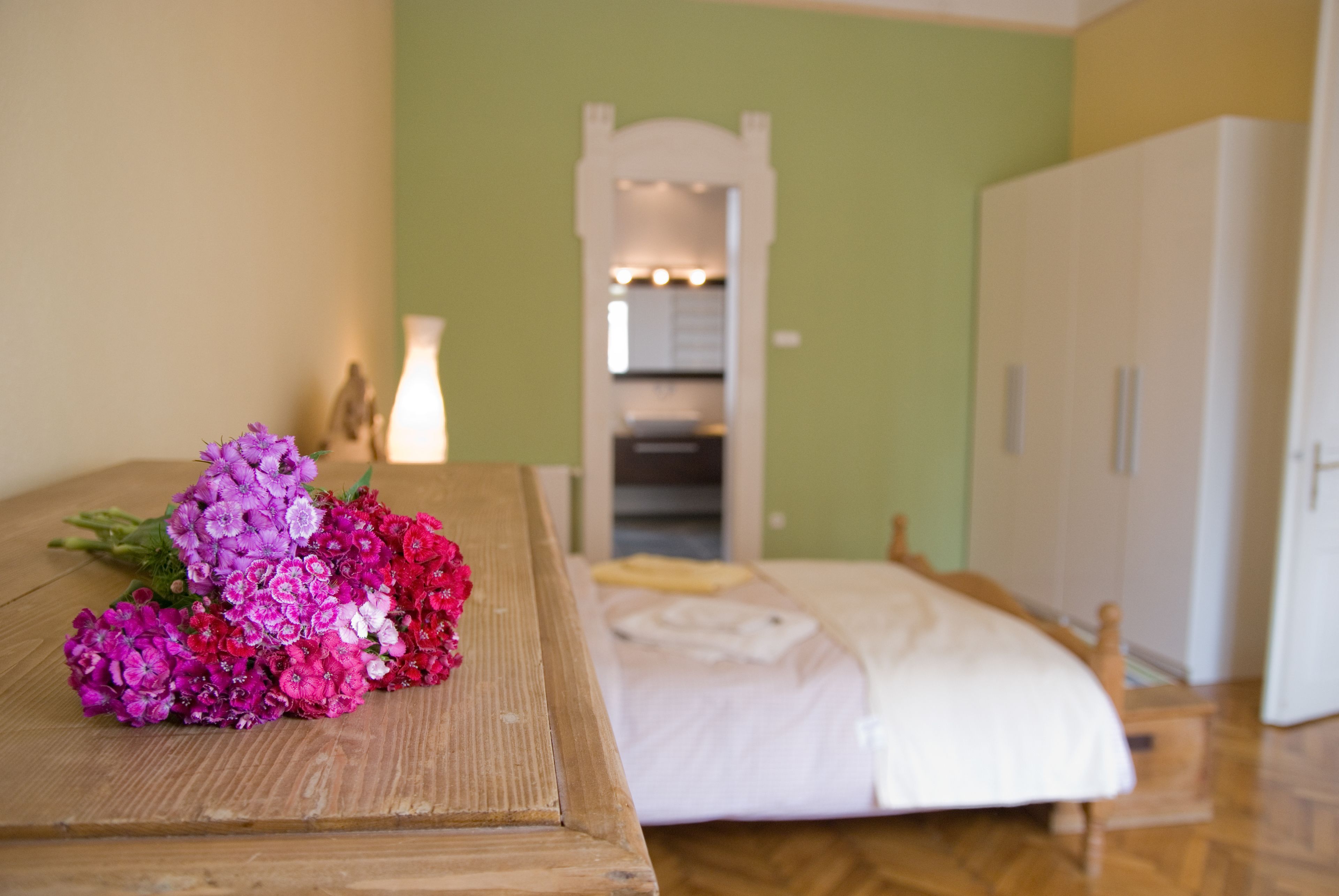 Ein Schlafzimmer mit einem hölzernen Bett, einem weißen Schrank und einem Spiegel mit Beleuchtung darüber.