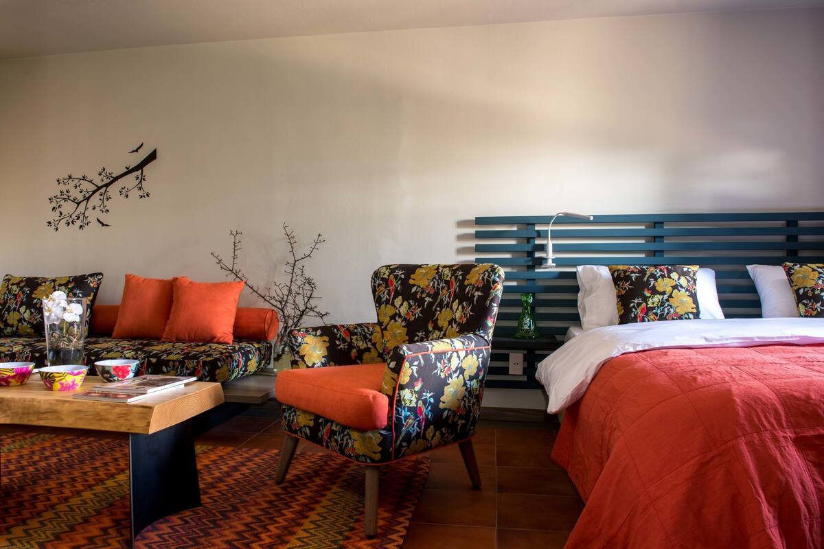 Een hotelkamer met een bank, stoel, bed en een muur met een tak en vogels.