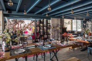 A dining area with wooden tables set for a meal, surrounded by bookshelves and decorative plants. - La Maison des Cèdres (Al Arz)