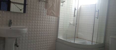 Casa de banho com lavatório branco, cabine de duche com vidro e sanita.