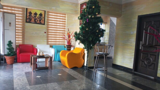 Un vestíbulo con un sofá rojo, un sillón amarillo, un sofá blanco, un árbol de Navidad y una puerta con un tirador decorativo.
