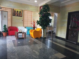 Un vestíbulo con un sofá rojo, un sillón amarillo, un sofá blanco, un árbol de Navidad y una puerta con un tirador decorativo.