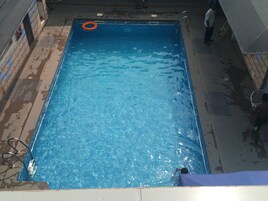 Una piscina rectangular con agua azul cristalina, un flotador salvavidas y una escalera.
