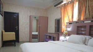 Un dormitorio con una cama, un armario, una silla, un escritorio, un espejo y una lámpara.