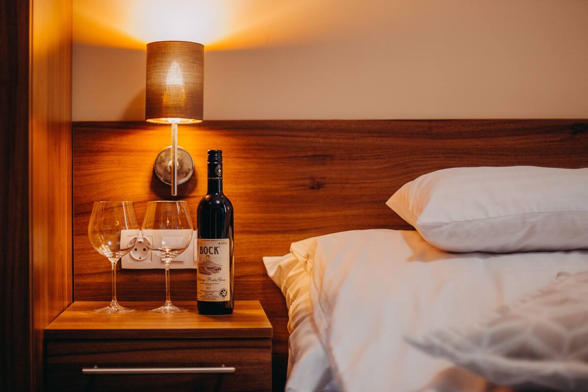 A wooden bedside table with a bottle of Bock wine and two empty wine glasses.