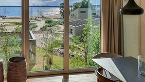 A room with a large window overlooking a beach and wind turbines, featuring a dining area with a table and chairs. - Beautiful apartment in Lembruch/Dümmer See with indoor swimming pool (Lembruch/Dümmer See)