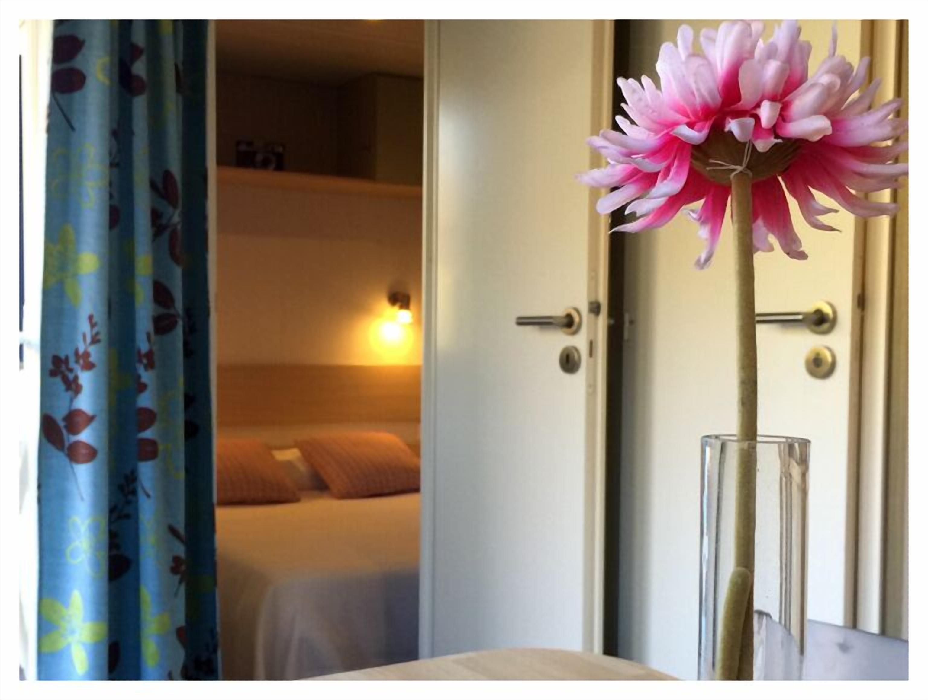 Una habitación con una cama, una puerta y un jarrón con una flor.
