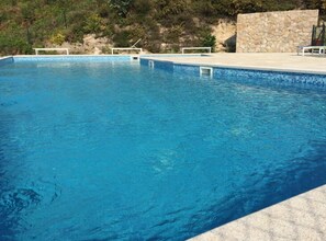 Una piscina de color blau clar amb una paret de pedra i una barana blanca.