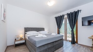 Een slaapkamer met een groot bed, een nachtkastje met lamp, een aan de muur bevestigde televisie en een raam met gordijnen.