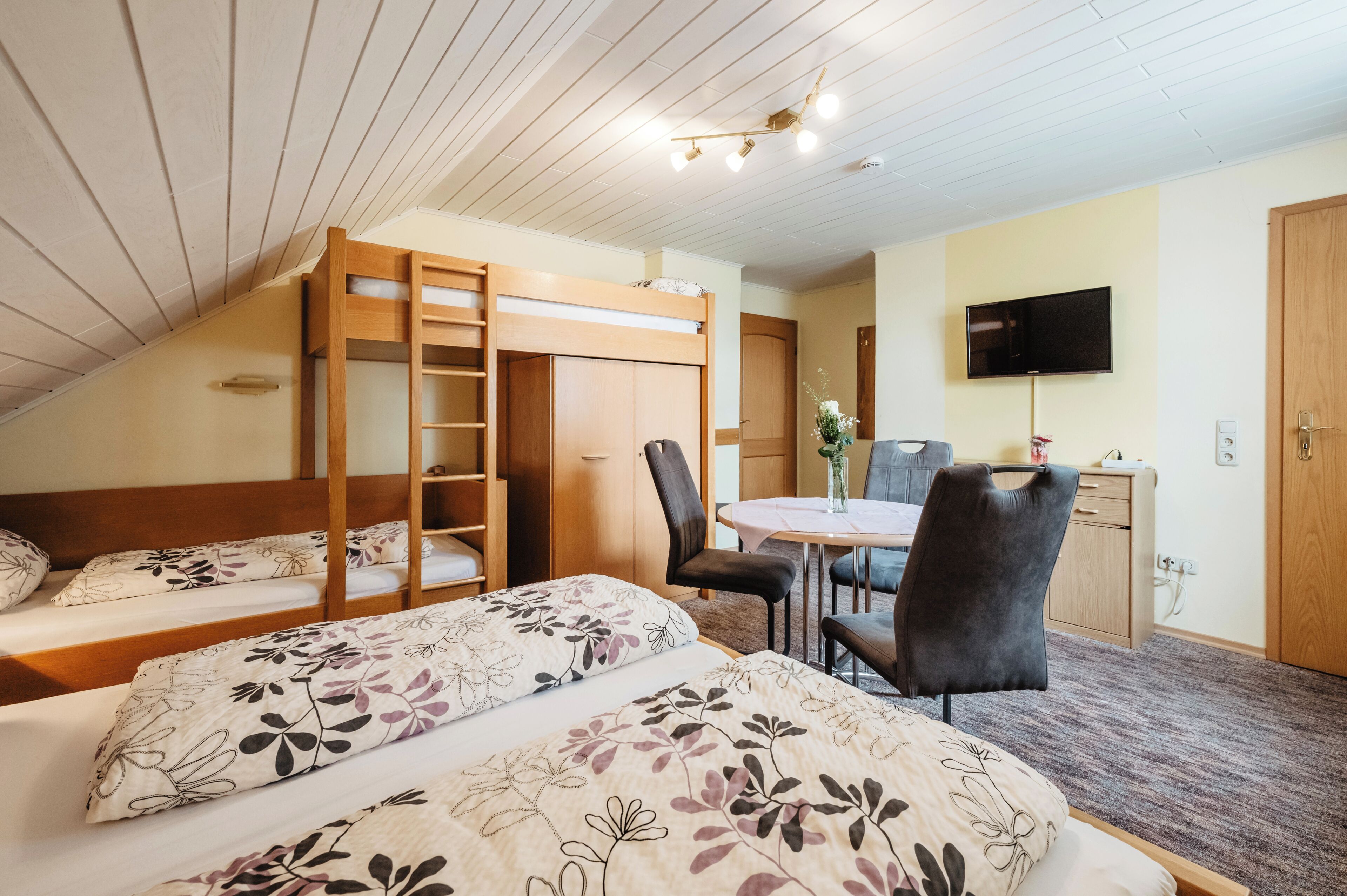 A room with two beds, a desk, a chair, a TV, and a wardrobe.