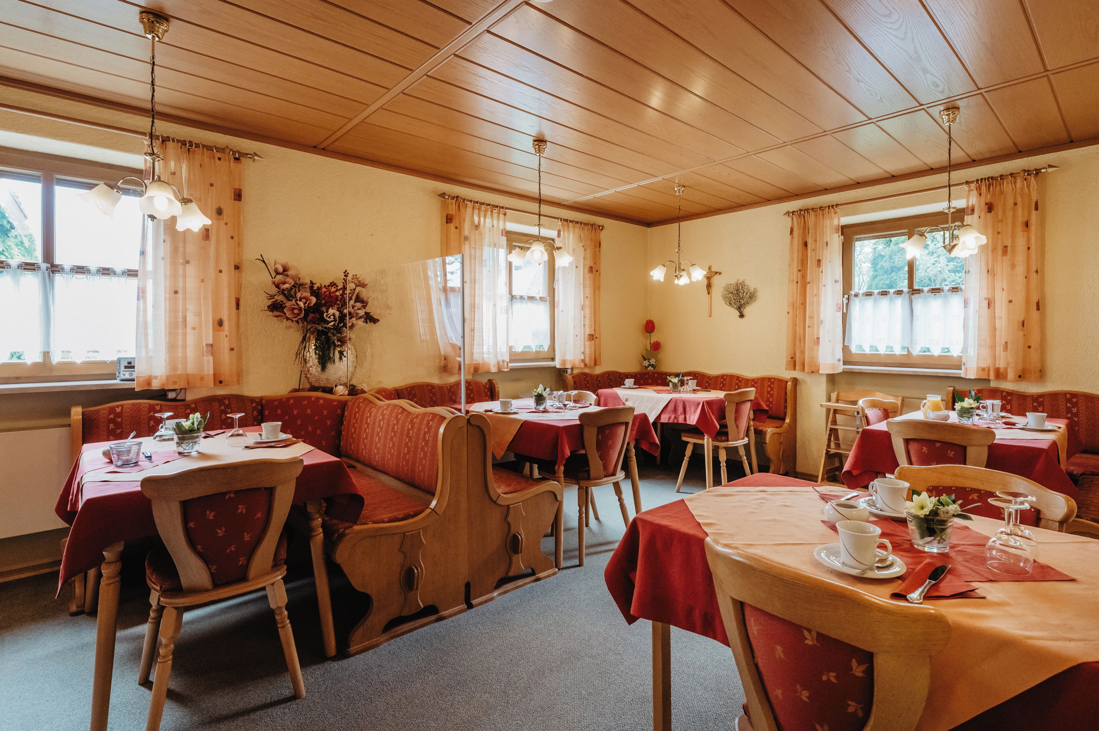Un ristorante con panche e tavoli in legno, apparecchiati con posateria e un vaso di fiori.