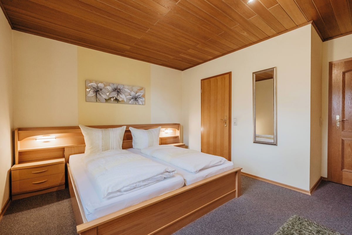 A bedroom with a wooden bed, bedside tables, a mirror, and a floral artwork on the wall.