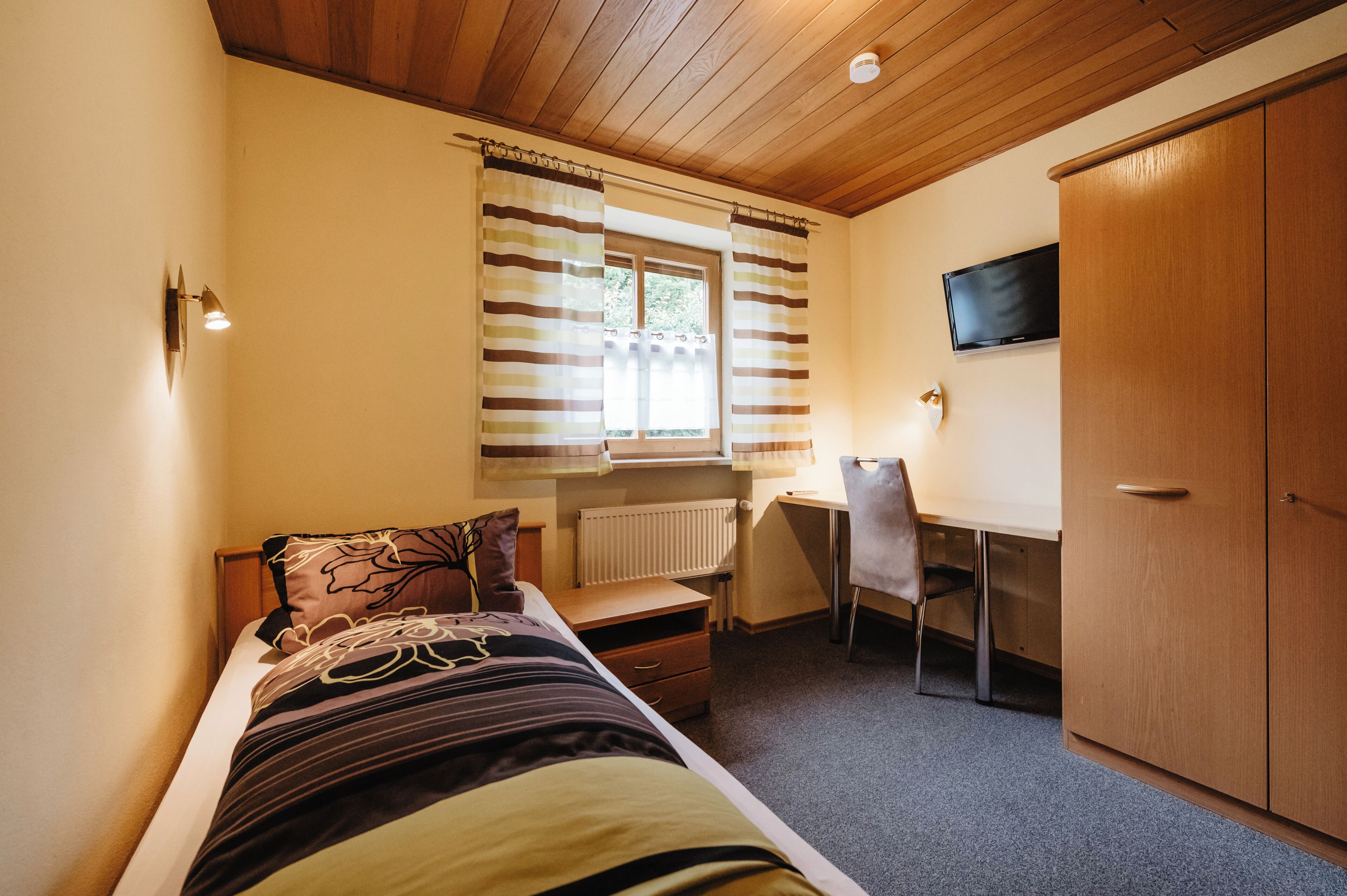 A bedroom with a bed, a desk, a chair, a TV, and a wardrobe.