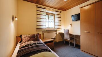 A bedroom with a bed, a desk, a chair, a TV, and a wardrobe.