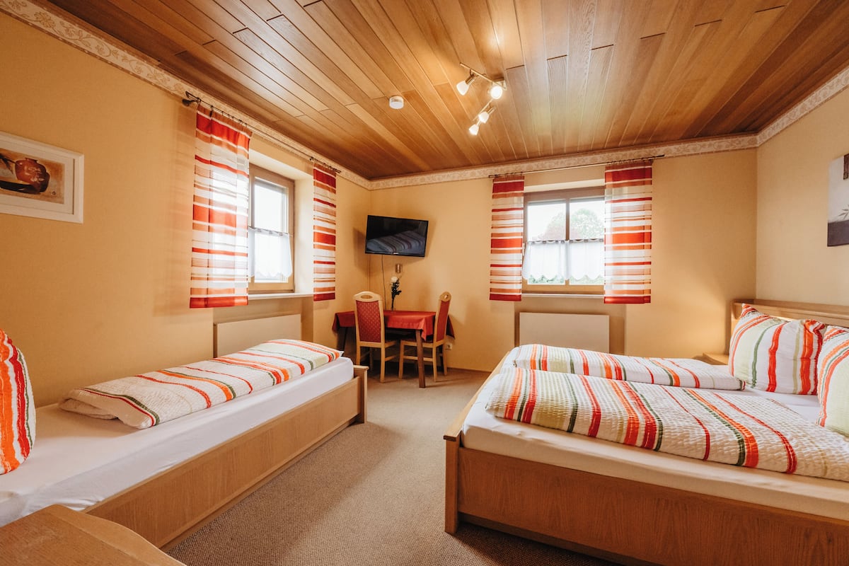 A room with two single beds, a small table, a chair, and a TV mounted on the wall.